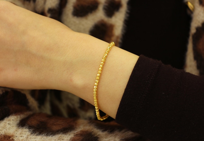 Puede incluir: Un brazalete de oro con un dise&ntilde;o texturizado y de cuentas.