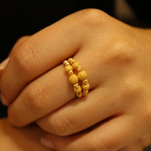 May include: A gold ring with a beaded design. The ring is worn on a person's finger.