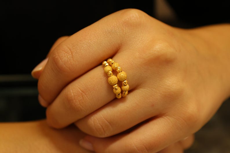 May include: A gold ring with a beaded design. The ring is worn on a person's finger.