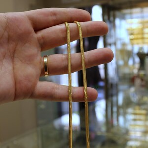 May include: A gold chain necklace with a snake chain design. The chain is held in a hand.