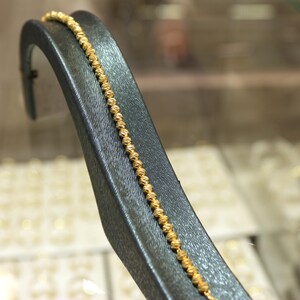 Puede incluir: Un brazalete de cadena de oro con un dise&ntilde;o texturizado. El brazalete se muestra en un soporte de terciopelo negro.