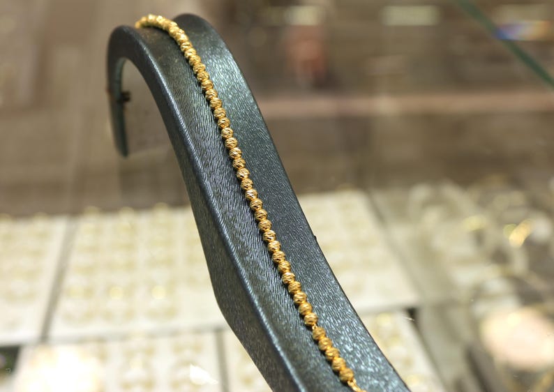 Puede incluir: Un brazalete de cadena de oro con un dise&ntilde;o texturizado. El brazalete se muestra en un soporte de terciopelo negro.