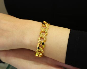May include: A gold chain bracelet with a thick, textured design. The bracelet is worn on a person's wrist.