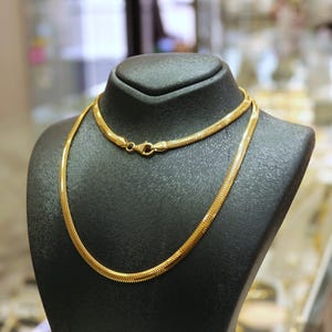 May include: Two gold chains on a black display stand. The chains are both snake chains, one is thicker than the other.