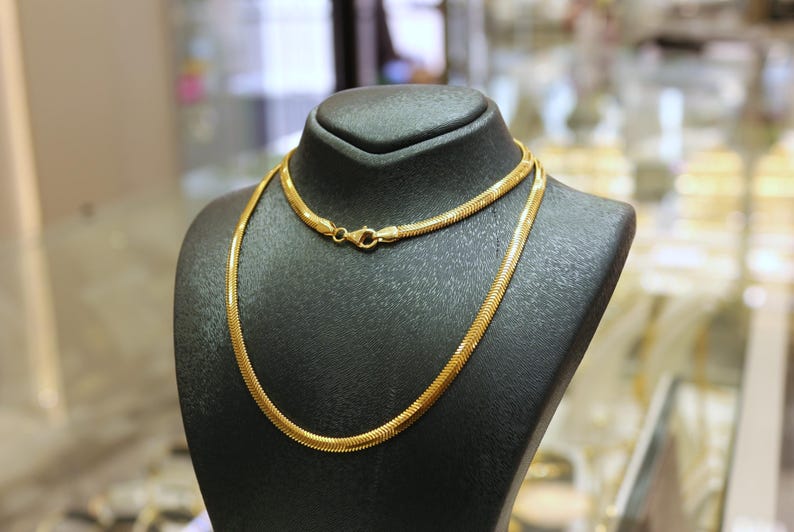 May include: Two gold chains on a black display stand. The chains are both snake chains, one is thicker than the other.