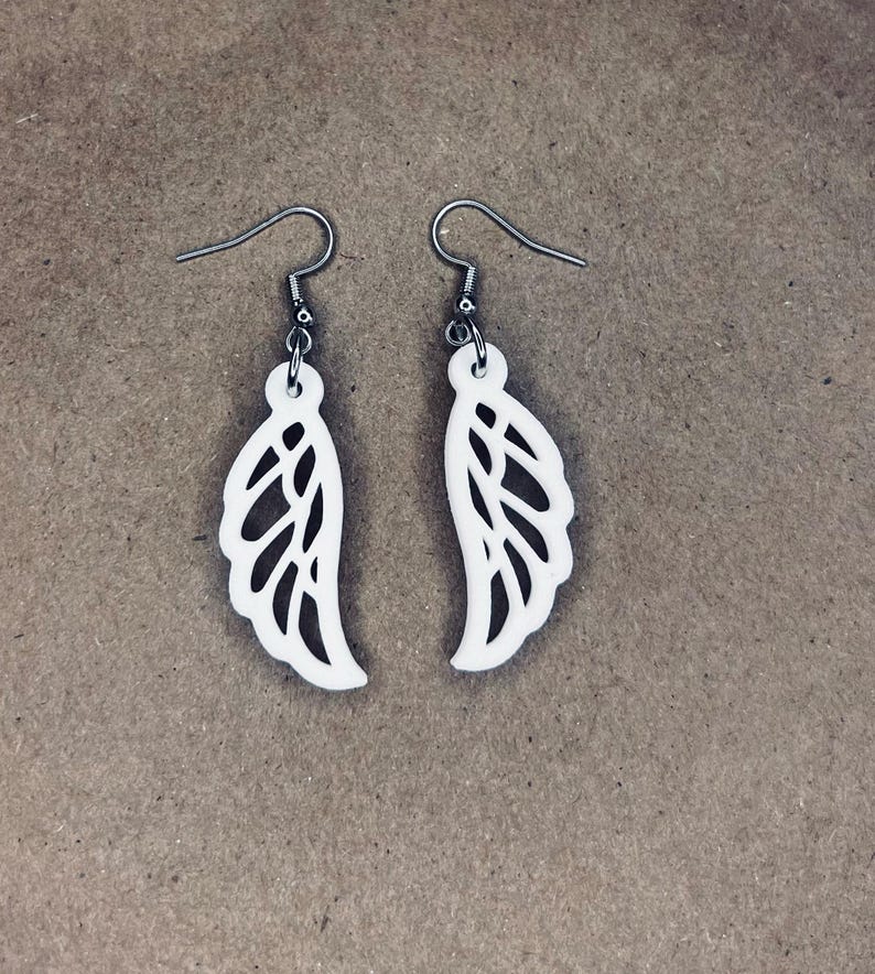 May include: A pair of white dangle earrings with a delicate wing design. The earrings are made of metal and have a silver hook.