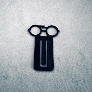 May include: Black plastic bookmark shaped like a pair of glasses with a long, thin rectangle for the bookmark part.