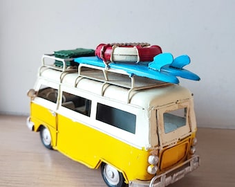 May include: A yellow and white vintage-style toy van with a surfboard, life preserver, and luggage on the roof rack.