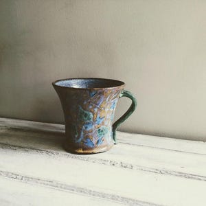 May include: A blue and green ceramic mug with a floral design. The mug has a handle and a wide base.