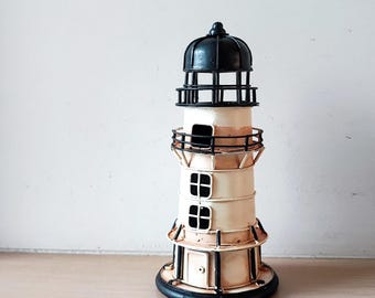 May include: A white and black metal lighthouse figurine with a black roof and a black base. The lighthouse has two windows and a small door.