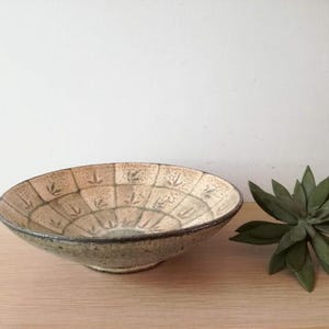 May include: A large, round, ceramic bowl with a white glaze and a green and brown pattern. The bowl has a wide rim and a slightly flared base.