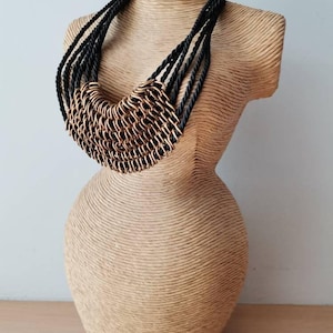 May include: A black rope necklace with a large, gold, chain-link pendant. The necklace is displayed on a mannequin.