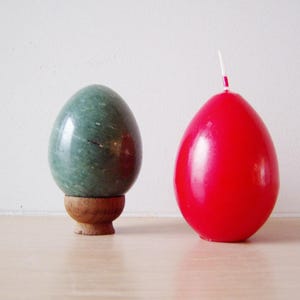 Könnte beinhalten: Ein grünes Marmor-Ei auf einem Holzständer neben einem roten Kerzen-Ei.