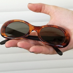 Puede incluir: Un par de gafas de sol ovaladas de carey marrón con patillas negras.