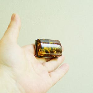 以下が含まれることがあります： 濃い茶色の半透明な長方形の琥珀のジュエリー。琥珀は自然で有機的な外観で、植物質のインクルージョンがあります。