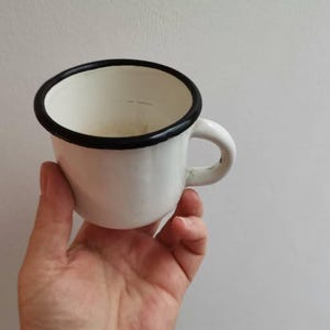 Vintage enameled mug, white enamel wäre drinking cup with black rim, early eighties