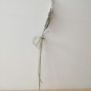 以下が含まれることがあります： 銀色のグリッター小麦の茎に、緑と白のリボンが結ばれています