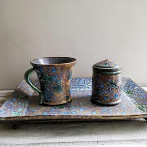May include: A ceramic tray with a blue and green floral pattern, featuring a matching mug and a small lidded jar.