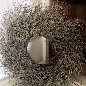 May include: A brown and green twig wreath with a natural, rustic look. The wreath is made of thin, dried twigs and has a simple, elegant design.