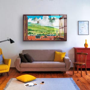 May include: A framed print of a window view with a picturesque landscape. The scene features a green valley with a small town in the distance, a blue sky with white clouds, and a brown wooden window frame.