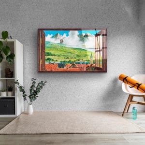 May include: A framed print of a window view with a cityscape and mountains in the distance. The window is open and the view is framed by a wooden window frame. The cityscape is made up of red-roofed buildings and a church steeple. The mountains are in the background and are covered in green grass and trees. The sky is blue and there are white clouds.