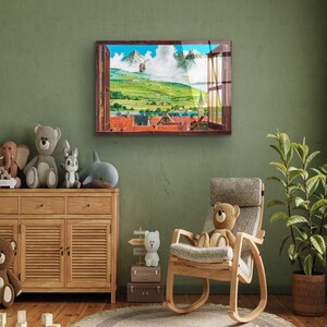 May include: A framed print of a window view with a colorful landscape scene. The window is open and the view shows a green field, a small town, and mountains in the distance. The print is hanging on a green wall above a wooden dresser.