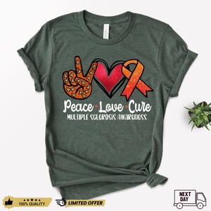 Puede incluir: Una camiseta verde oscuro con un signo de paz, un coraz&oacute;n y una cinta naranja. El texto "Peace Love Cure" y "Multiple Sclerosis Awareness" est&aacute; impreso en la camiseta.