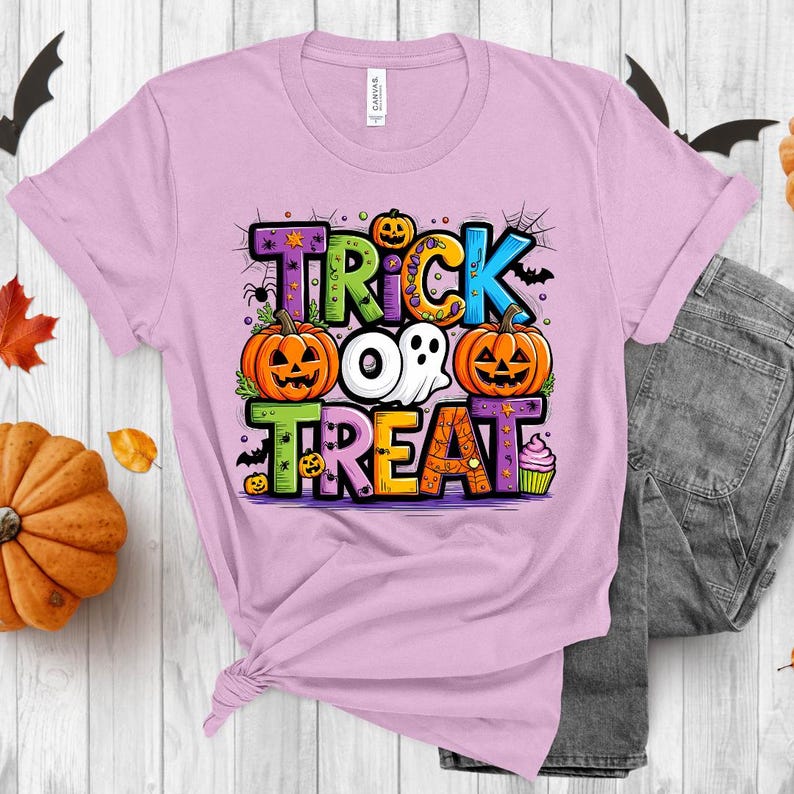 May include: A pink t-shirt with a colorful graphic that says "Trick or Treat" with pumpkins, a ghost, and a cupcake.