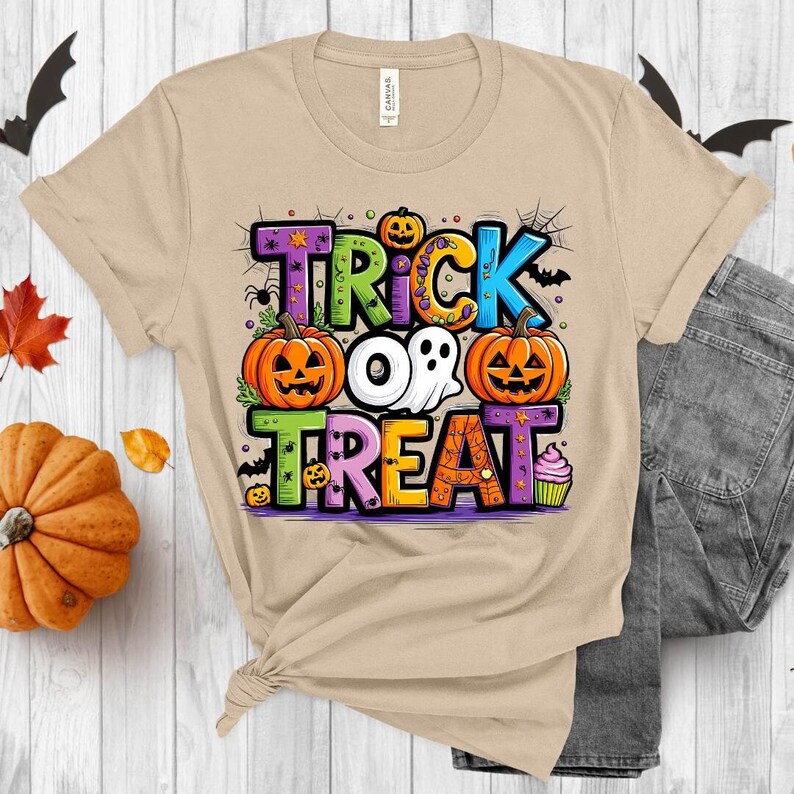 May include: A tan t-shirt with a colorful "Trick or Treat" graphic featuring pumpkins, ghosts, bats, and candy. The graphic is surrounded by stars and spiderwebs.