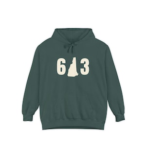 May include: A dark green hoodie with a front pocket and a drawstring hood. The hoodie features the number "603" in a cream color, with the outline of the state of New Hampshire in the center.