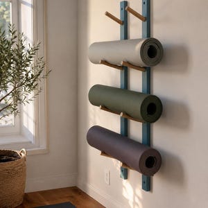 May include: A wall-mounted yoga mat rack featuring two vertical blue wooden rails with three pairs of light-coloured wooden pegs. Three rolled yoga mats in light grey, olive green, and dark charcoal are resting horizontally on the wooden pegs.