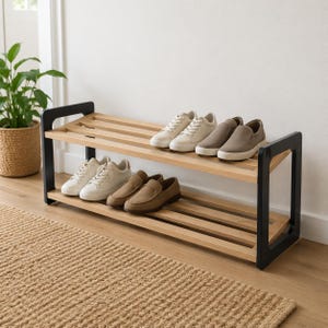 May include: A two-tier shoe rack featuring light wood slats and black metal side frames. The top shelf holds two pairs of light-colored sneakers and slip-on shoes, while the bottom shelf holds a pair of white sneakers and brown loafers.