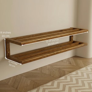 May include: A two-tiered wooden shelf, stained in a warm brown hue, mounted on a wall. The top shelf measures 12-47 inches (30-120 cm) in length, while the lower shelf is 12 inches (30 cm) wide. The shelf is 8 inches (20 cm) high.
