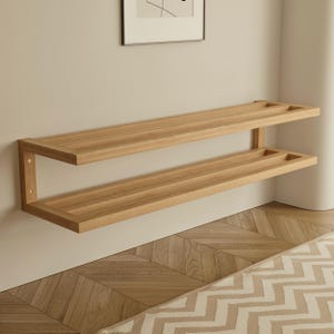 May include: A two-tiered, light-colored wooden wall shelf. The shelves are rectangular with a recessed area on each end. The shelf is mounted on a light-colored wall. The wood grain is visible. The shelf is a modern design.