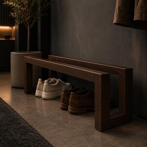 May include: A dark brown wooden shoe rack with two levels, holding pairs of shoes. The shoes include white sneakers and brown leather shoes. A potted plant and a dark wall are in the background.