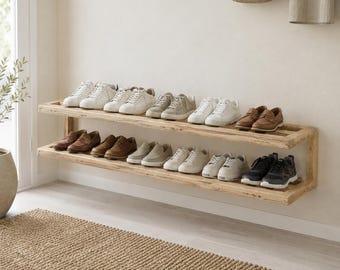 May include: A wall-mounted shoe rack made of light-coloured wood, with two shelves holding an assortment of shoes. The shoes are in white, beige, brown, and black. A woven rug is on the floor beneath the rack.