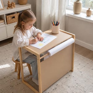 Könnte beinhalten: Ein Kinderschreibtisch aus hellem Holz mit integriertem Papierrollenhalter an der Seite, einer flachen Tischplatte und einem passenden kleinen Holzhocker. Der Schreibtisch ist für Zeichen- und Schreibaktivitäten konzipiert und enthält einen Stiftehalter.