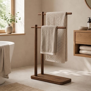 Può includere: Un portasciugamani in legno scuro a due livelli, con due asciugamani beige. Il supporto ha una base rettangolare. Gli asciugamani hanno trame diverse, uno a nido d'ape e uno liscio. Circa 70 cm di altezza.