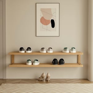 May include: A wooden shoe rack with two shelves, displaying various pairs of shoes. The shoes include sneakers and heels in neutral colors. An abstract art print hangs above the rack, adding a decorative touch to the entryway.