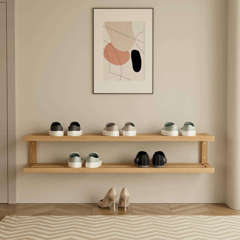 May include: A wooden shoe rack with two shelves, displaying various pairs of shoes. The shoes include sneakers and heels in neutral colors. An abstract art print hangs above the rack, adding a decorative touch to the entryway.