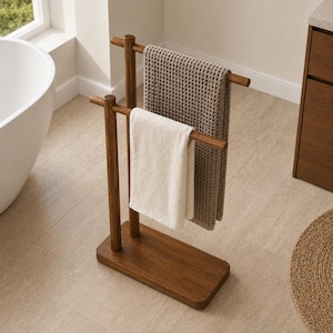 Op de afbeelding: Een houten handdoekenrek met twee horizontale stangen, met een beige wafelhanddoek en een witte handdoek. Het rek is gemaakt van donker hout en heeft een rechthoekige basis. De badkameromgeving omvat een wit bad en een raam.