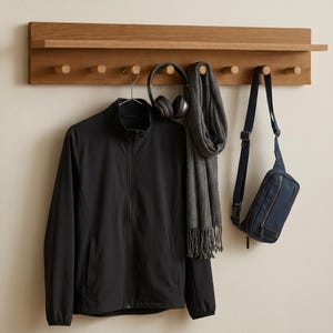 Könnte beinhalten: Eine Wandgarderobe aus Holz mit einem Regal und sechs Haken. Eine schwarze Jacke, ein grauer Schal, eine marineblaue Umhängetasche und Kopfhörer hängen an der Garderobe. Die Garderobe ist aus hellbraunem Holz.
