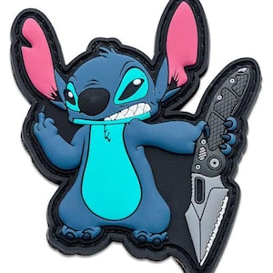 May include: A blue cartoon character patch with large pink ears and a turquoise belly, holding a gray knife. The character has a black nose and is set against a black background with a black border.