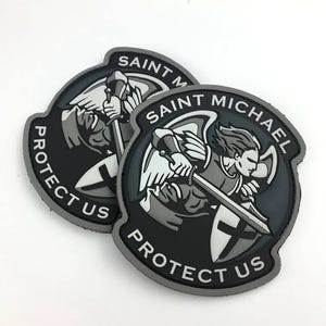 May include: Two black and gray Saint Michael patches. Each patch features an illustration of Saint Michael with a sword and shield, with the text "SAINT MICHAEL PROTECT US" in white.
