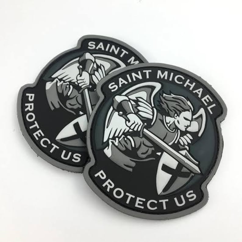 May include: Two black and gray Saint Michael patches. Each patch features an illustration of Saint Michael with a sword and shield, with the text "SAINT MICHAEL PROTECT US" in white.