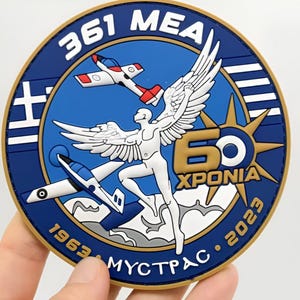 Può includere: Una toppa rotonda con sfondo blu raffigurante una figura alata bianca, due aerei e la scritta "361 MEA". La toppa include anche la scritta "60 XPONIA 1963 - 2023 MYCTPAC". Il design incorpora elementi della bandiera greca.