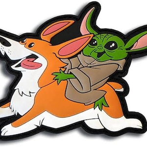 May include: A colorful patch featuring a corgi dog carrying a green alien-like character. The corgi is orange and white with a pink tongue, while the alien is green with large ears and a brown cloak. The patch has a black border.