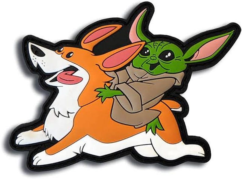 May include: A colorful patch featuring a corgi dog carrying a green alien-like character. The corgi is orange and white with a pink tongue, while the alien is green with large ears and a brown cloak. The patch has a black border.