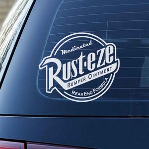 May include: A black car's rear window features a white and black sticker. The sticker says "Medicated Rust-eze Bumper Ointment Rear End Formula" in a circular design. The car's taillights are red.