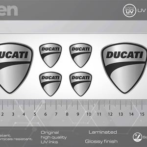 May include: Six silver and black vinyl stickers with the word "DUCATI" in a stylised font. The stickers are 5.5 cm in diameter and are designed for use on motorcycles, cars, or other surfaces.